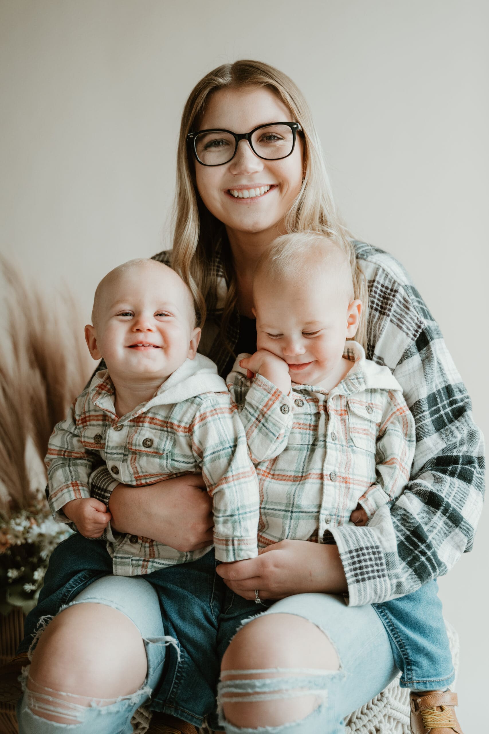 Mom of twins holding them on her lap, all are in coordinating flannels and jeans.