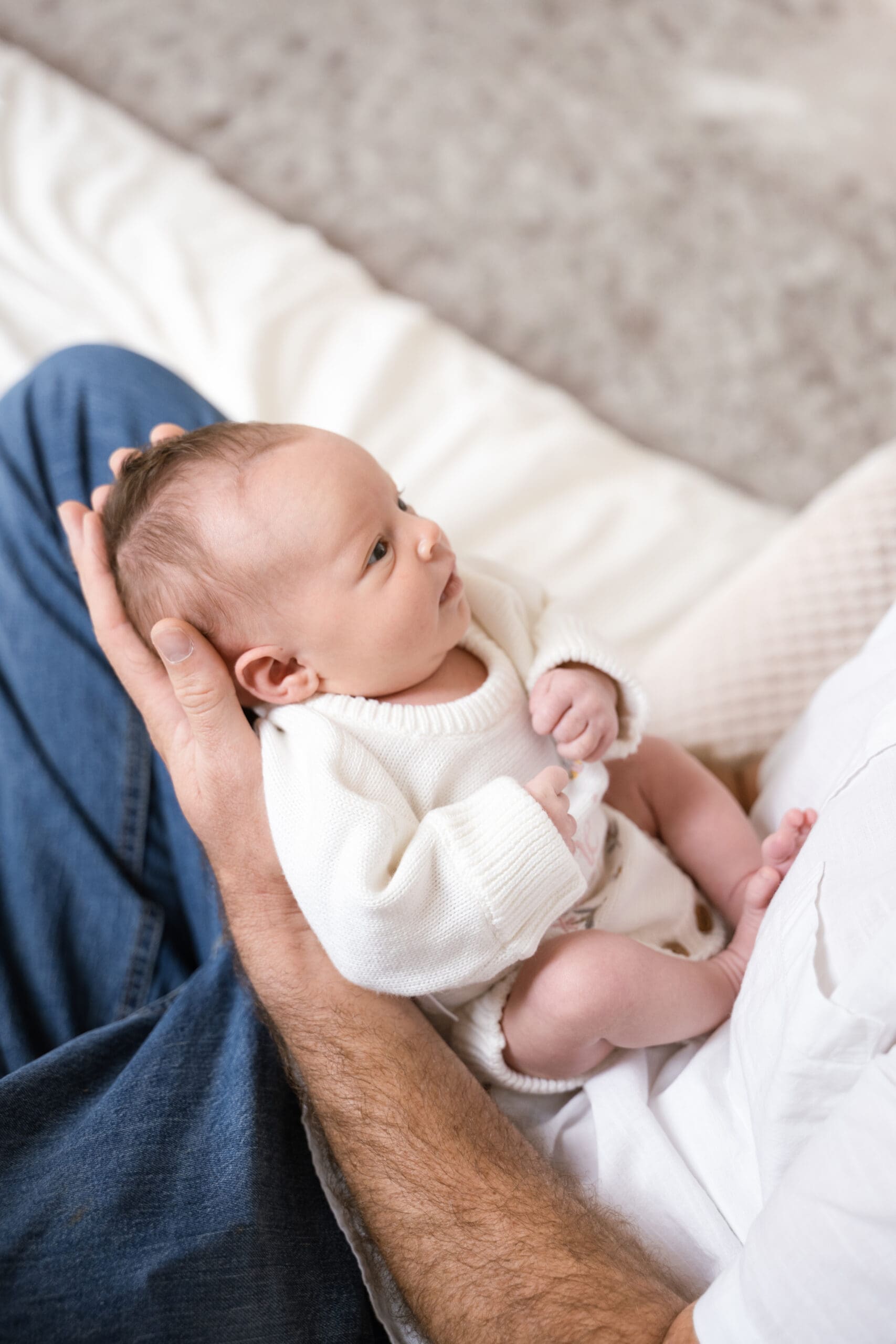 Image of a baby in a white sweater being cradled by her father's hands.