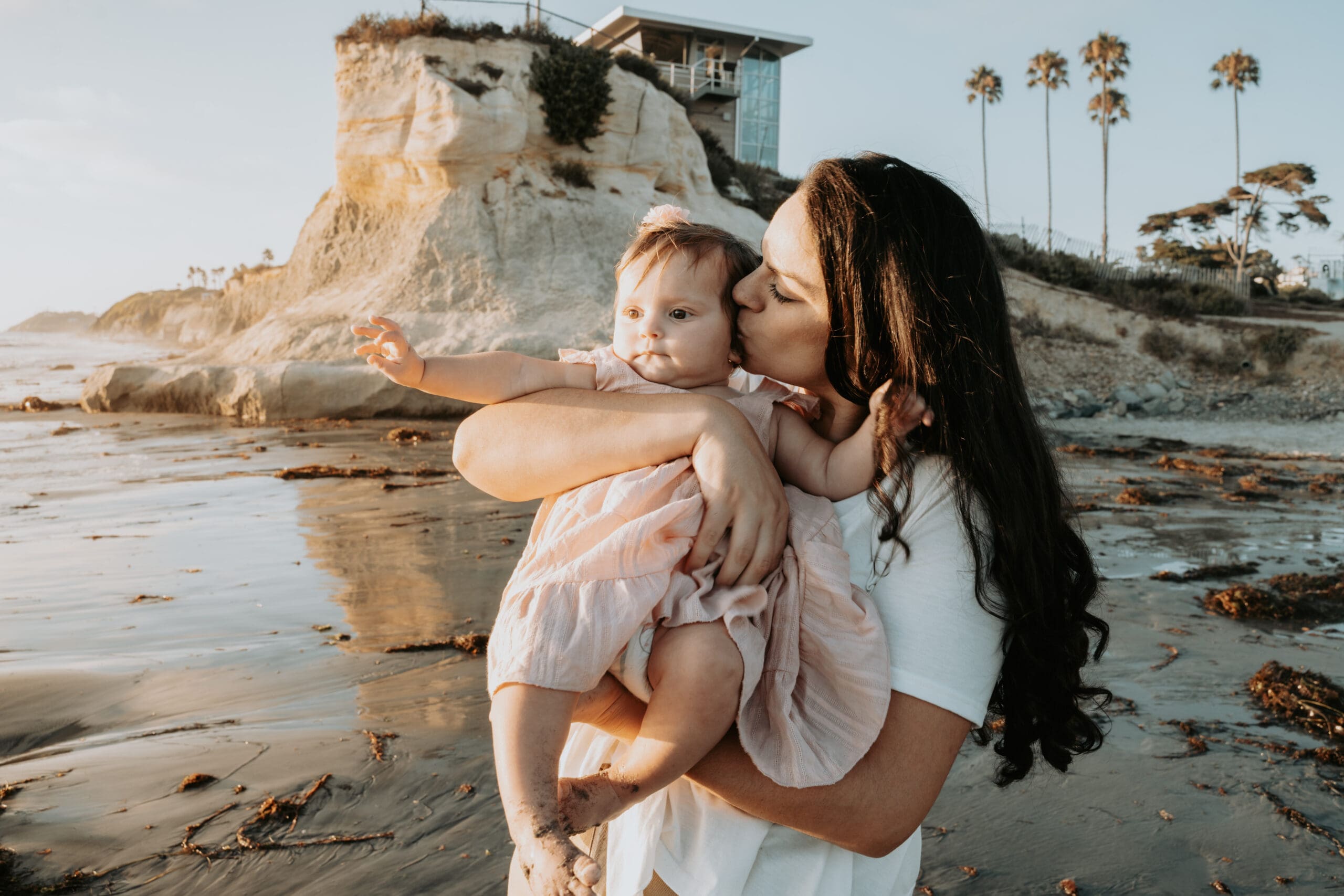 Picture of a mother holding her daughter and kissing her on the cheek on the beach.