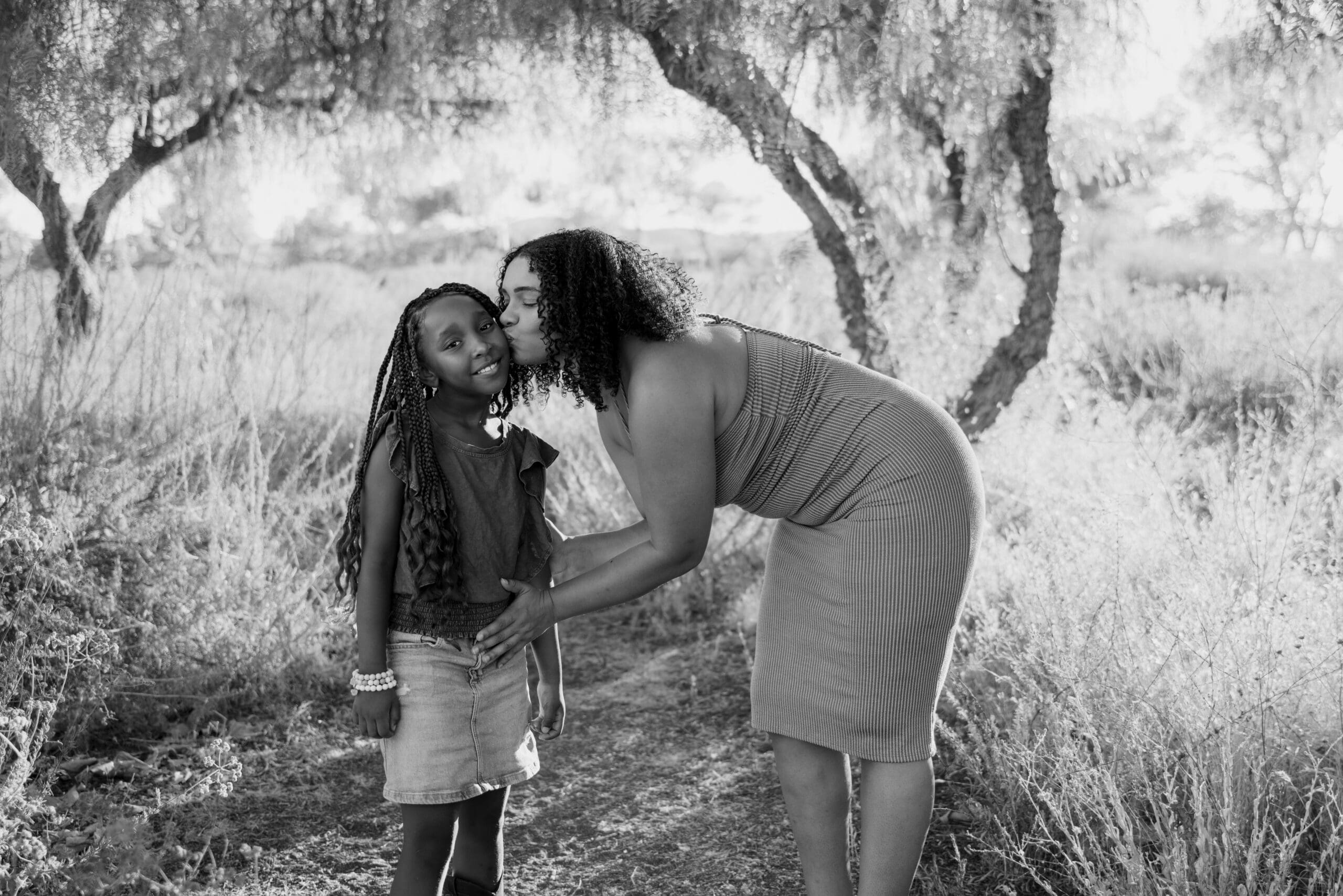 Photo of mom kissing daughter on the cheek in woods in black and white.